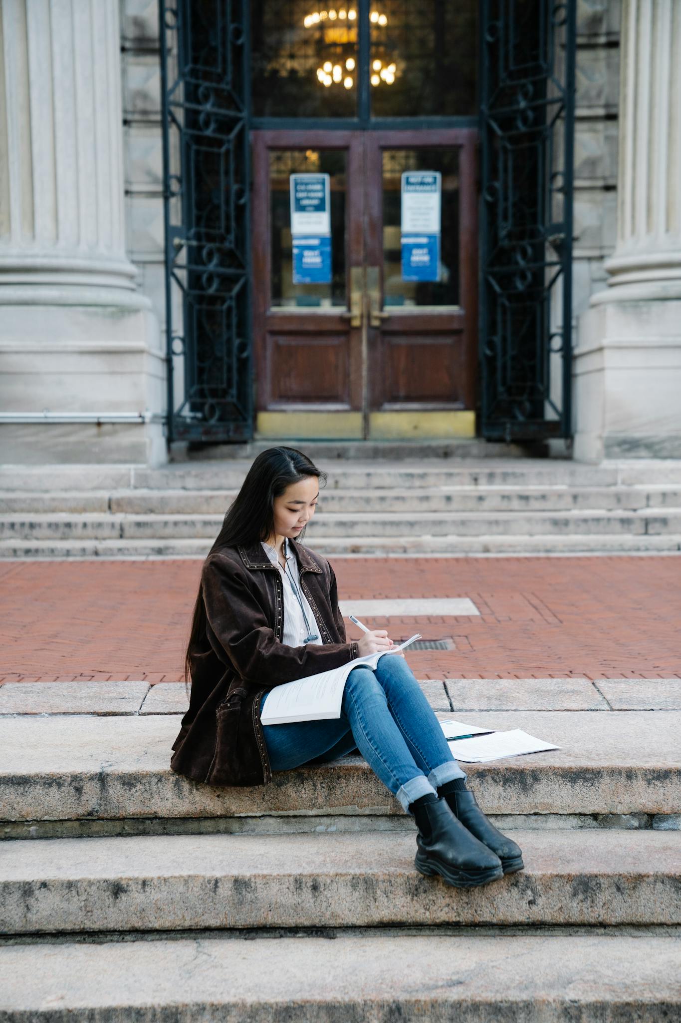 A female student sits studying on the steps of a historic campus building.