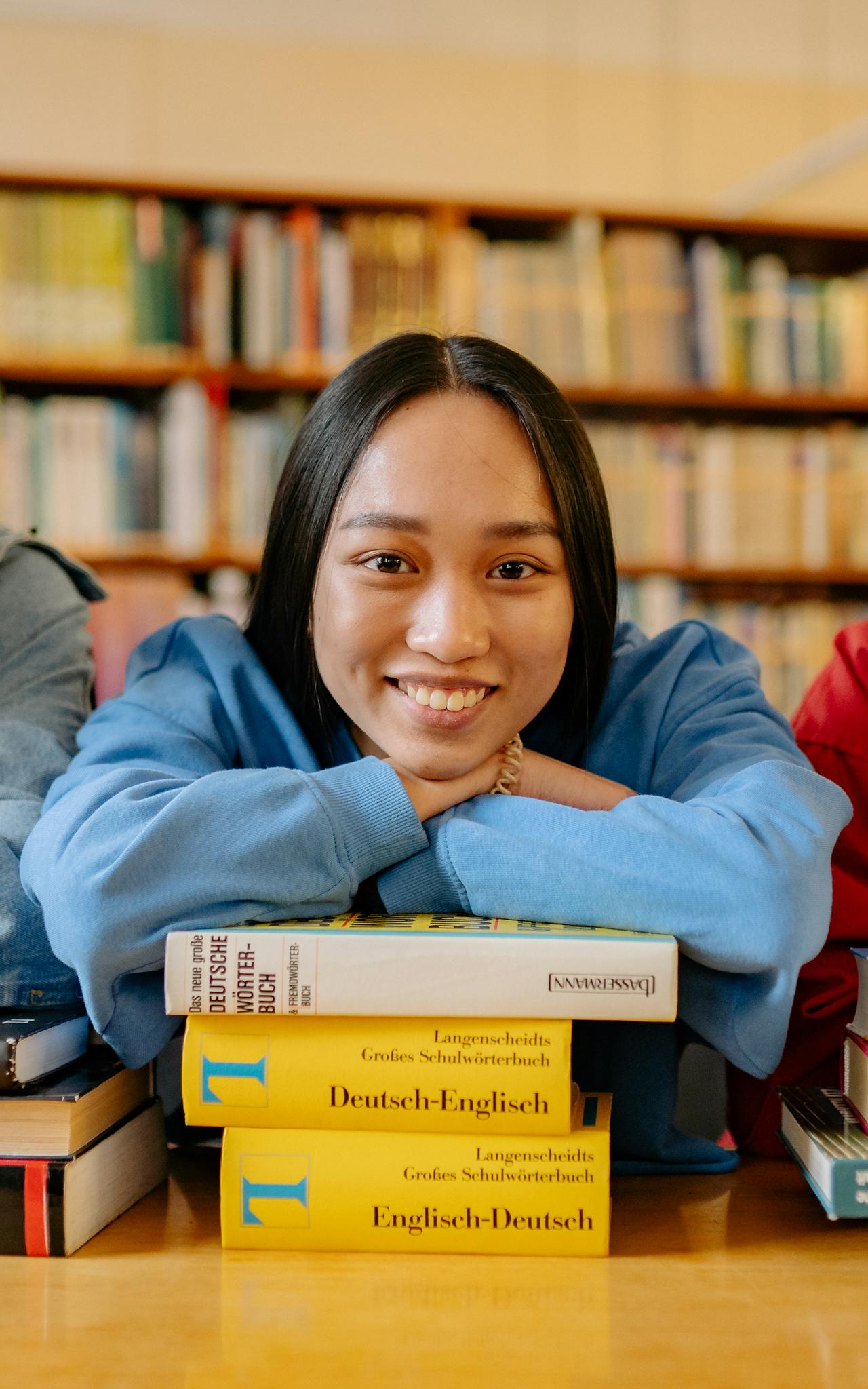Smiling student in a library leaning on a stack of books, symbolizing education and learning.