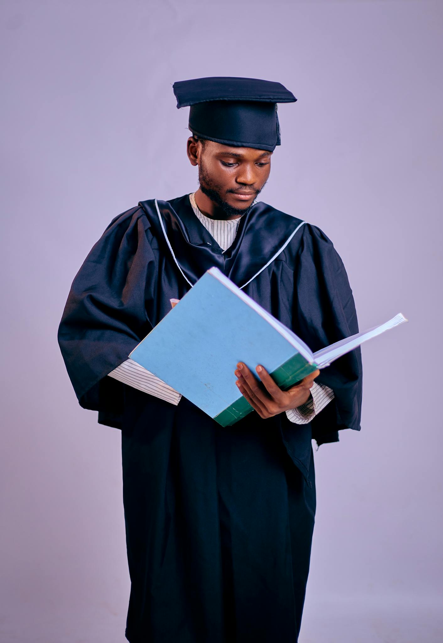 Young graduate in cap and gown reading a book, symbolizing education success.